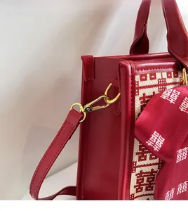 Detail of a red leather bag featuring a gold metal hook and traditional Xi pattern