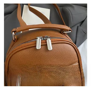 Close-up of brown litchi leather backpack featuring silver metal dual zippers and handle
