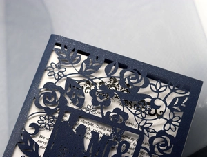 Macro detail of laser-cut rose vines on a navy blue matte wedding invitation cover