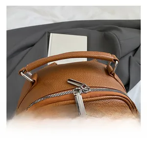 Close-up of brown litchi leather backpack featuring reinforced top handle and silver zippers