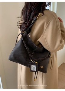 Detail of dark brown suede tote bag with woven knot handle worn over a wool coat