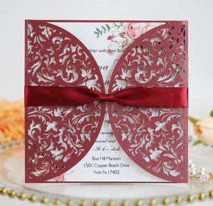 Detail of burgundy laser-cut wedding invitation with elegant satin ribbon on a decorative tray