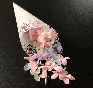 Detail of white laser-cut heart pattern cone with colorful dried flower petals for weddings