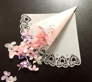 Macro shot of white laser-cut lace wedding cone with heart patterns and dried flower petals