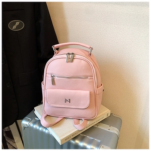 Pink PU leather backpack with dual zippers and metal logo shown on a silver suitcase