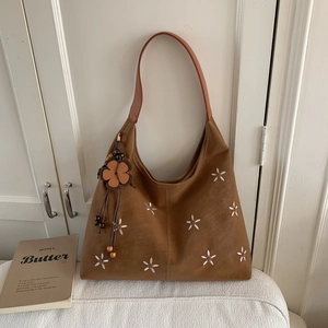 Détail du sac cabas en daim marron avec broderie florale blanche et pendentif fleurie
