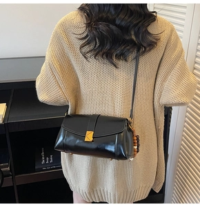 Detail of black glossy leather crossbody bag with gold triangle lock and beaded charm