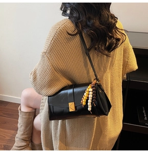 Close-up of black glossy leather bag with gold triangle clasp and wood bead charm