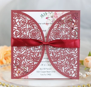Detailed laser cut rose patterns on burgundy wedding invitation with red silk ribbon bow