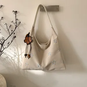 Détail du sac à bandoulière crème avec broderies florales bleues et breloque en perles