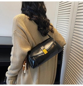 Detail of black patent leather crossbody bag with gold triangle clasp and beaded tassel