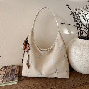 Détail de broderie florale sur sac hobo crème avec breloque en perles de bois