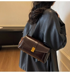 Detail of dark brown leather crossbody bag with gold buckle and wooden bead charm
