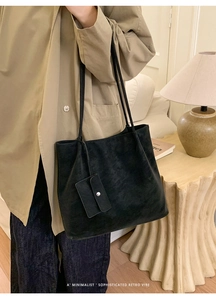 Minimalist black matte tote bag with small pouch shown on shoulder in cozy room