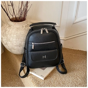 Close-up of black litchi grain texture and silver metal logo on fashion backpack