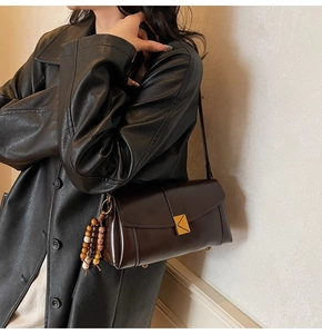 Detail of chocolate brown leather crossbody bag with golden triangular clasp and bead charm