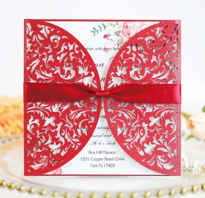Detail of red laser-cut wedding invitation featuring a butterfly pattern and satin ribbon bow