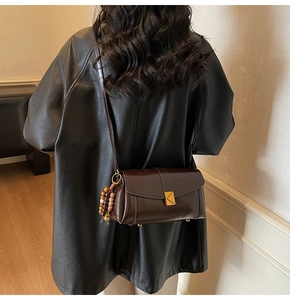 Detail of dark brown glossy leather crossbody bag with gold buckle and beaded charm accessory