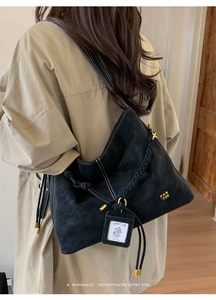 Detail of black textured leather hobo bag with braided handle and gold metal hardware