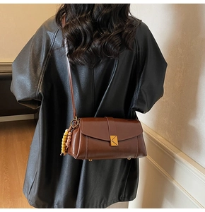 Detail of a brown PU leather crossbody bag with gold buckle and beaded charm on a model