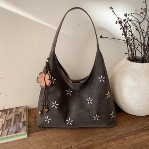 Détail du sac hobo en daim gris avec broderie florale et pendentif à pompon