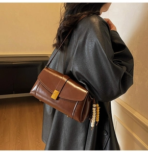 Detailed shot of brown leather crossbody bag with gold triangle clasp and wooden bead tassel