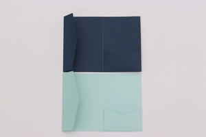 Detail view of craft paper invitations featuring navy blue and light green folders with pockets