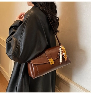 Detail of a brown leather crossbody bag featuring a gold buckle and wood bead strap ornament