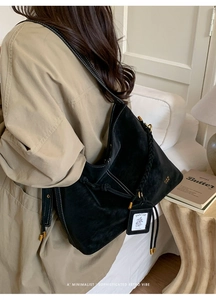 Detail of black suede tote bag with white contrast stitching and woven handle on shoulder