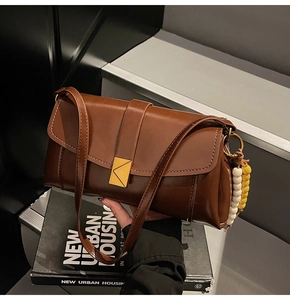Detail of dark brown leather crossbody bag with gold triangle clasp and beaded charm