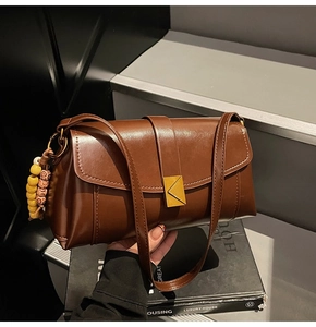 Detail of vintage brown leather handbag with gold triangle buckle and wooden bead charm