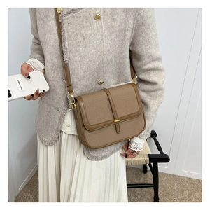 Detail view of a brown leather saddle bag paired with a tweed jacket and pleated skirt