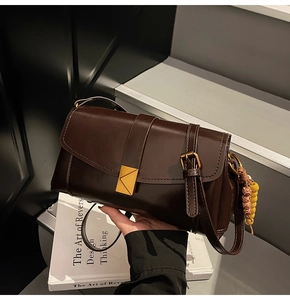 Close-up of retro brown leather crossbody bag with gold buckle and beaded charm detail
