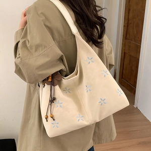 Détail de la broderie florale et du pompon perlé sur le sac cabas beige porté