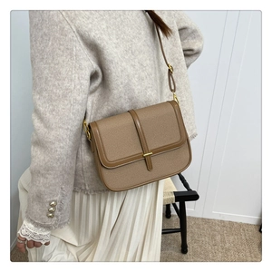 Close-up of brown textured crossbody bag styled with a grey blazer and white skirt