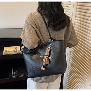 Detail view of large black tote bag featuring textured faux leather and rabbit plush charm