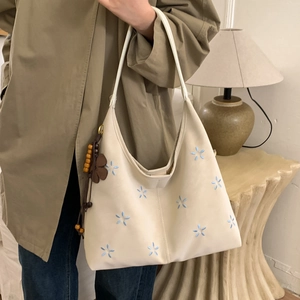 Détail de la broderie florale et du pendentif en bois sur le sac fourre-tout