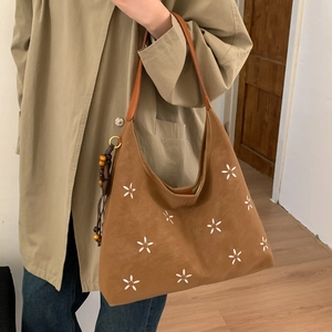 Détail d'un sac cabas marron avec broderie florale blanche et pendentif à pampilles en bois