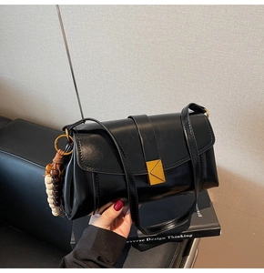 Detail of black vintage shoulder bag with golden triangle clasp and wooden bead charm