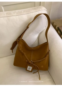Detail of a brown matte leather hobo bag with a woven lanyard and decorative brand tag