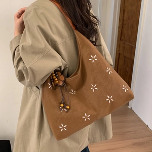 Gros plan d'un sac hobo en daim marron avec broderie florale blanche et breloque en bois