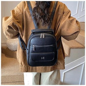 Detail of black pebbled leather backpack with silver zippers and M logo on a model