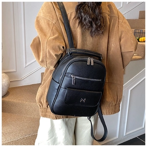 Detail of black lychee grain leather backpack with silver zippers and metal logo on stairs