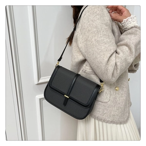 Detailed side view of the black textured leather flap bag worn with a tweed coat