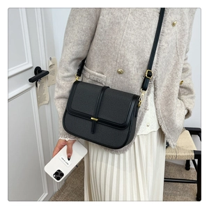 Detail showing the black textured fabric crossbody bag with elegant gold buckle on a model