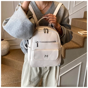 Close-up of cream backpack with litchi grain PU leather and silver metal logo detail