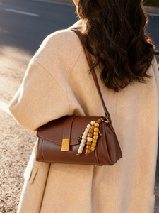 Vintage brown leather crossbody bag with gold buckle and beaded charm in soft sunset light