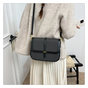 Side view of a black square crossbody bag worn by a model in a minimalist home setting