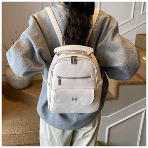 Rear view of model wearing a cream pebbled leather mini backpack with metal logo detail