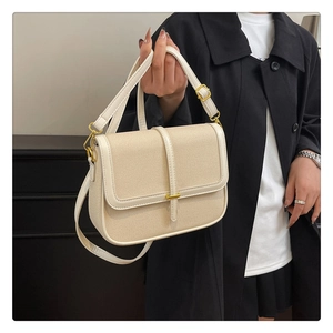 Detail of beige textured fabric crossbody bag with creamy leather trim and gold metal bar